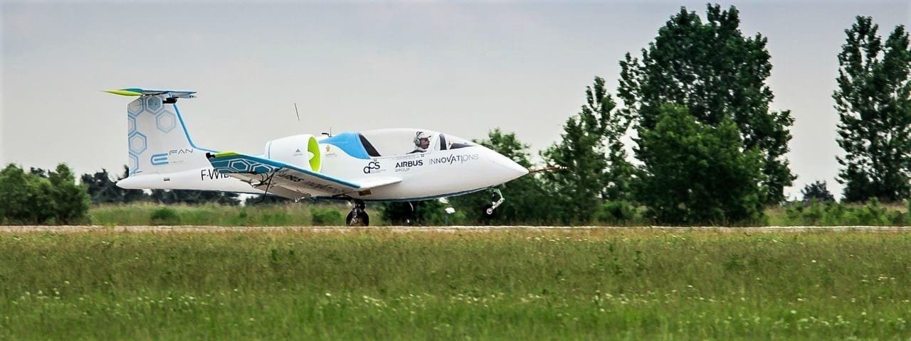 An Airbus E-Fan taking off from a small runway surrounded by countryside